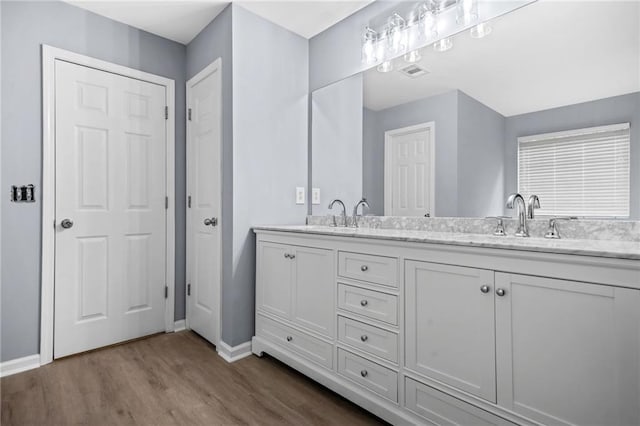 bathroom with baseboards, visible vents, a sink, double vanity, and wood finished floors