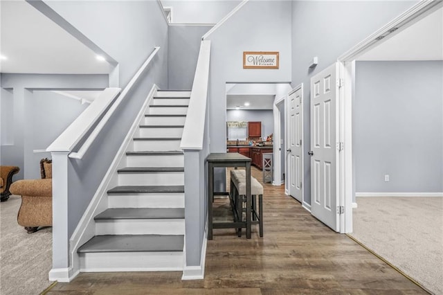 stairway featuring a towering ceiling, baseboards, recessed lighting, and wood finished floors