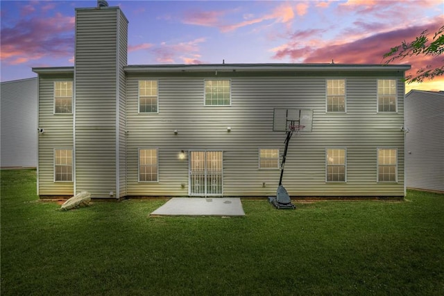 back of house at dusk with a yard, a patio area, and a chimney