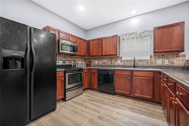 kitchen featuring dark countertops, a sink, black appliances, light wood-style floors, and tasteful backsplash