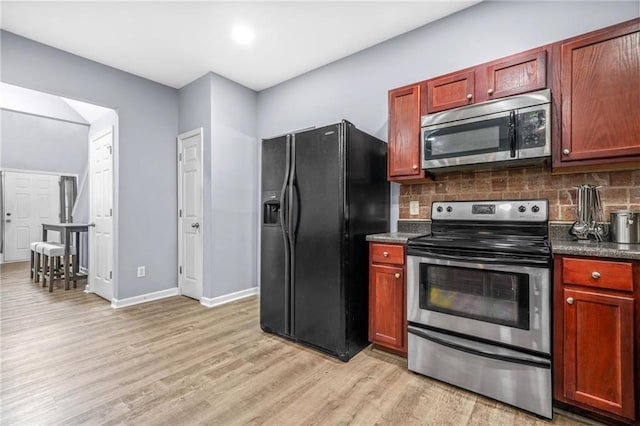 kitchen with light wood-style floors, backsplash, dark countertops, and appliances with stainless steel finishes