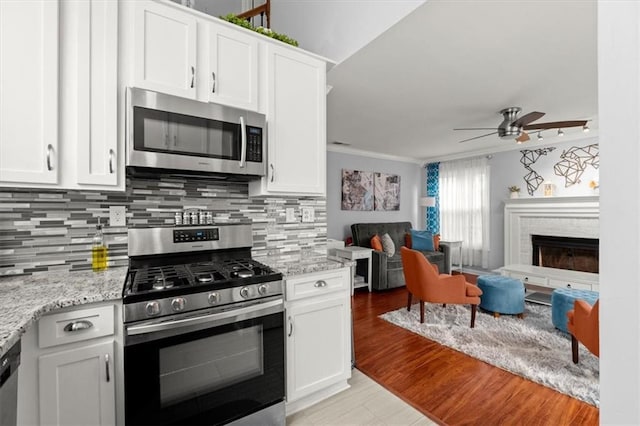 kitchen with stainless steel appliances, a brick fireplace, white cabinetry, and light stone counters