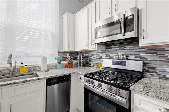 kitchen with light stone countertops, sink, stainless steel appliances, backsplash, and white cabinets