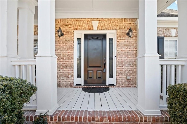 view of exterior entry featuring a porch, brick siding, and a shingled roof