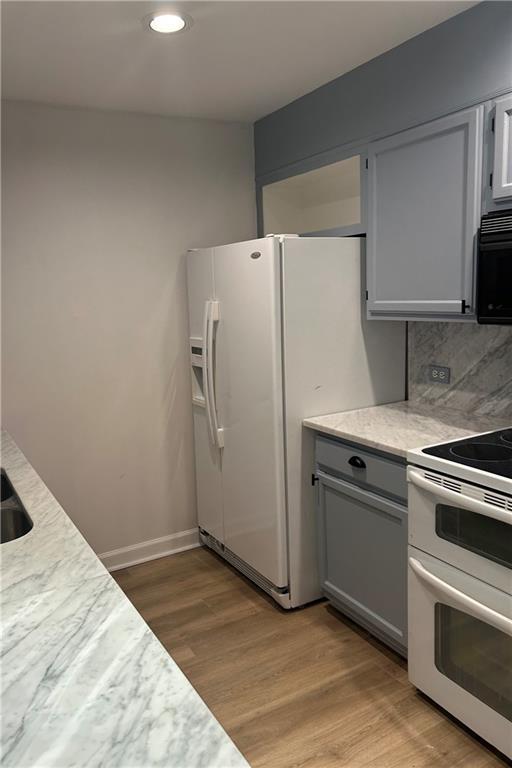 kitchen featuring tasteful backsplash, gray cabinets, light countertops, light wood-style flooring, and white appliances