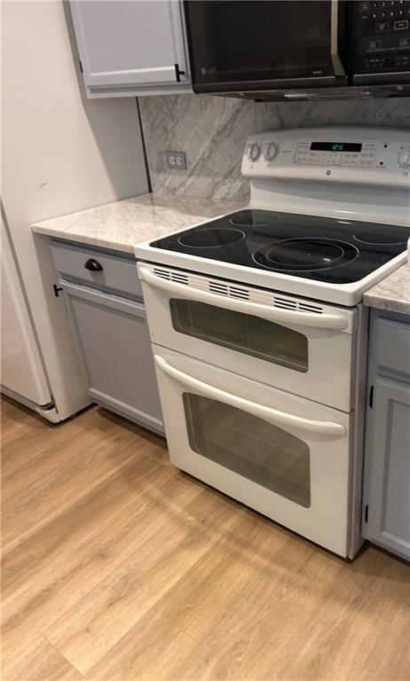 kitchen featuring range with two ovens, gray cabinets, light wood-style floors, black microwave, and backsplash