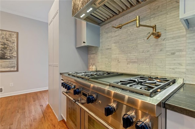 kitchen featuring crown molding, high end stainless steel range, backsplash, white cabinetry, and light hardwood / wood-style floors