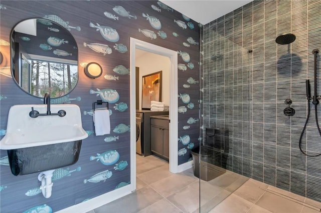 bathroom featuring sink, tiled shower, washer / dryer, and tile patterned flooring