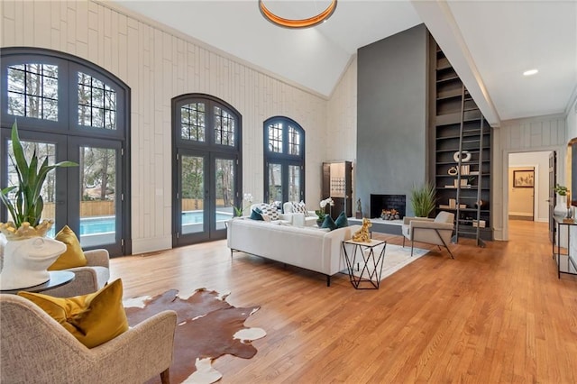 living room with light hardwood / wood-style floors, wood walls, french doors, and a fireplace