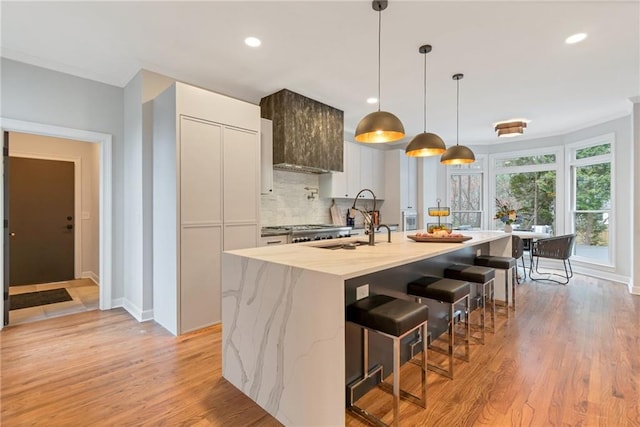 kitchen with tasteful backsplash, white cabinets, sink, light stone counters, and a center island with sink