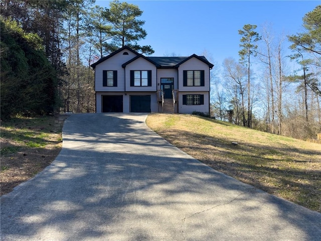 raised ranch featuring a garage, driveway, and a front lawn