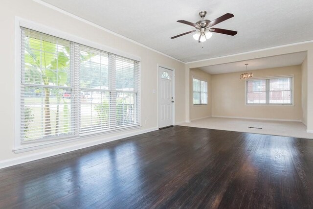 spare room featuring crown molding, ceiling fan with notable chandelier, a healthy amount of sunlight, and dark hardwood / wood-style floors