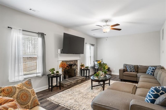 living room featuring a stone fireplace, dark hardwood / wood-style floors, and ceiling fan