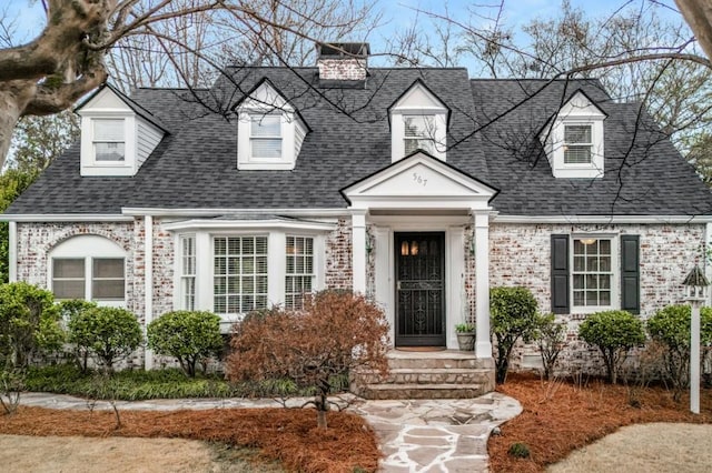 new england style home featuring brick siding and roof with shingles