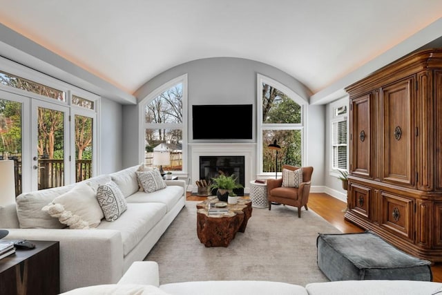 living room with light wood finished floors, a glass covered fireplace, baseboards, and vaulted ceiling