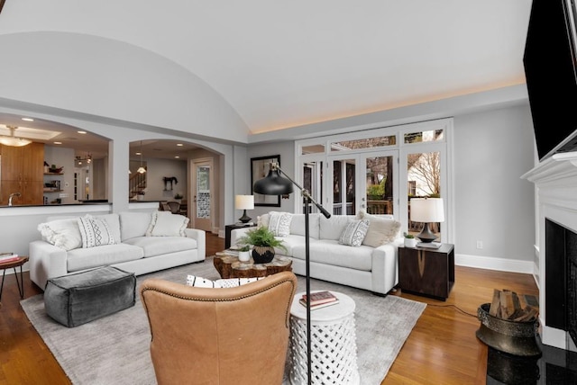 living area with wood finished floors, baseboards, lofted ceiling, a fireplace, and arched walkways