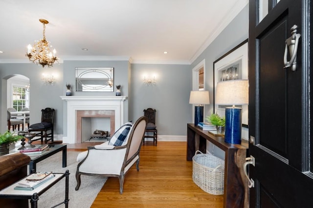 living area featuring light wood-style flooring, ornamental molding, arched walkways, a fireplace, and a chandelier