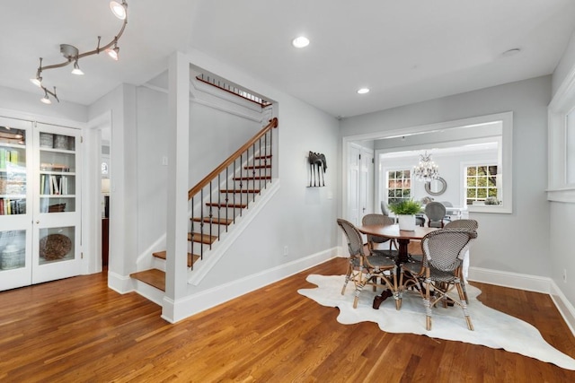 dining space featuring a notable chandelier, stairway, baseboards, and wood finished floors