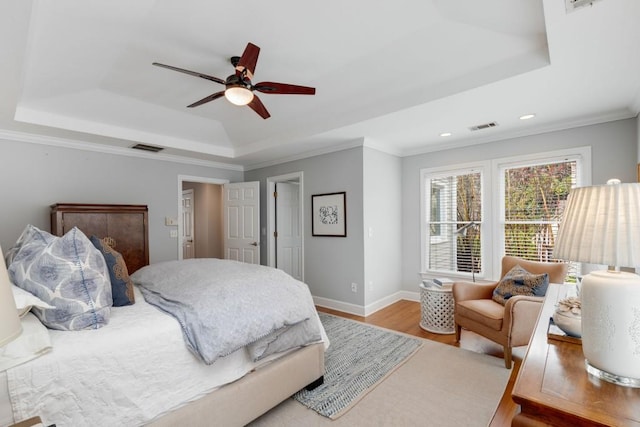 bedroom featuring visible vents, baseboards, a tray ceiling, and wood finished floors