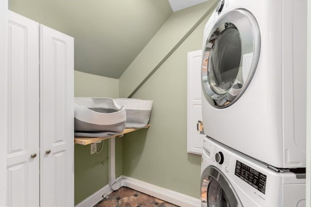 washroom with cabinet space, baseboards, and stacked washing maching and dryer