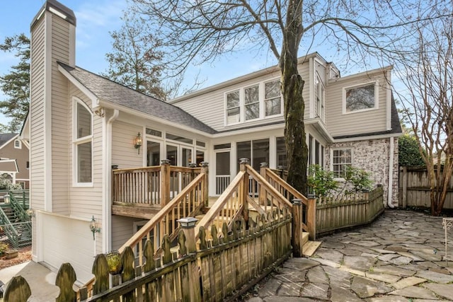 rear view of property with fence, a sunroom, a chimney, a garage, and a deck