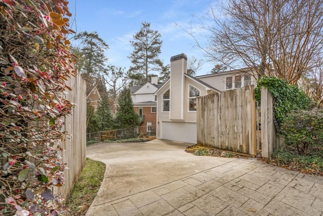 view of side of property with a chimney, an attached garage, concrete driveway, and fence