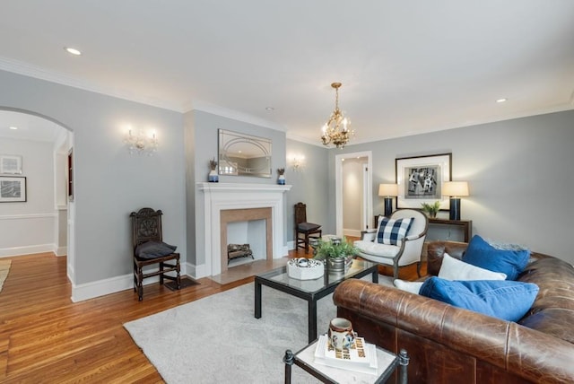 living room with a fireplace with flush hearth, wood finished floors, arched walkways, crown molding, and baseboards