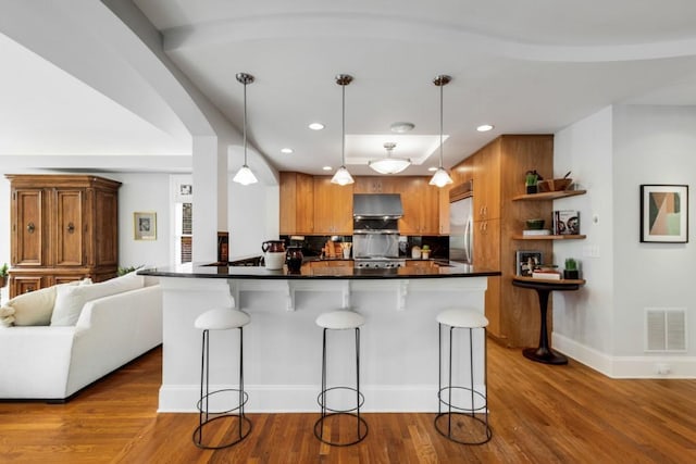 kitchen featuring range hood, visible vents, open shelves, brown cabinets, and stainless steel built in refrigerator