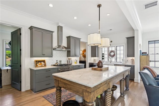 kitchen with crown molding, light wood-style floors, gray cabinets, wall chimney exhaust hood, and tasteful backsplash