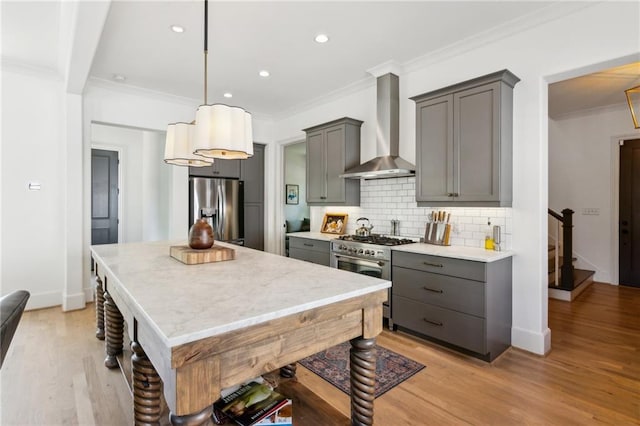 kitchen with decorative backsplash, gray cabinets, crown molding, stainless steel appliances, and wall chimney exhaust hood