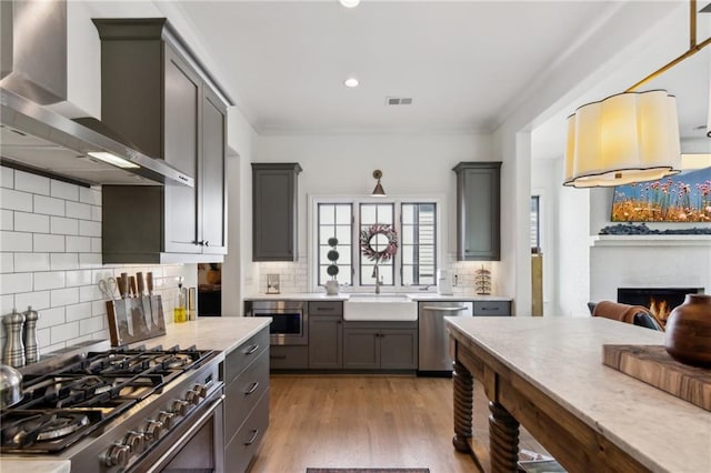 kitchen with light countertops, wall chimney exhaust hood, a sink, backsplash, and stainless steel appliances