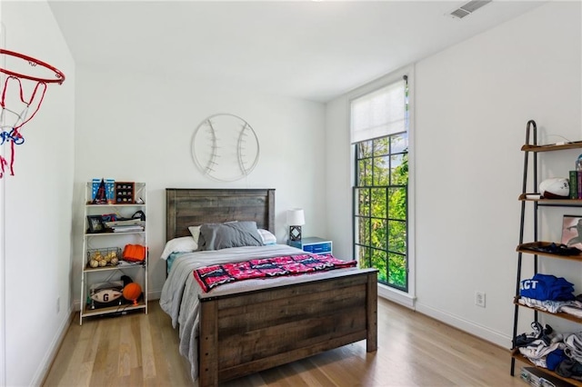bedroom with baseboards, visible vents, and wood finished floors