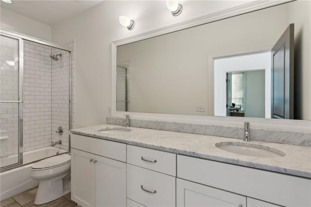bathroom featuring a sink, combined bath / shower with glass door, toilet, and double vanity