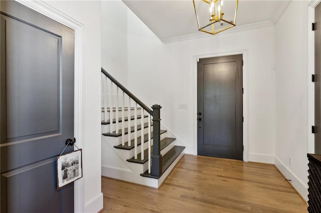 foyer featuring crown molding, a chandelier, baseboards, wood finished floors, and stairway