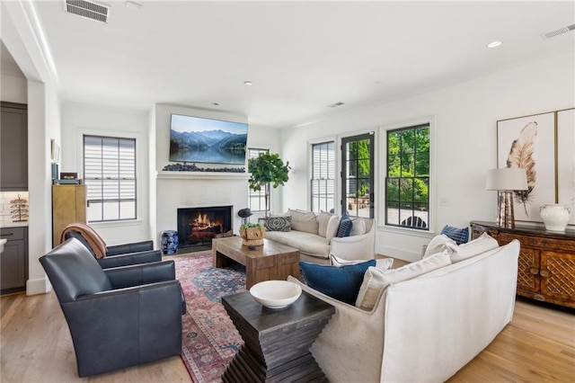 living area featuring light wood-style floors, recessed lighting, a warm lit fireplace, and visible vents
