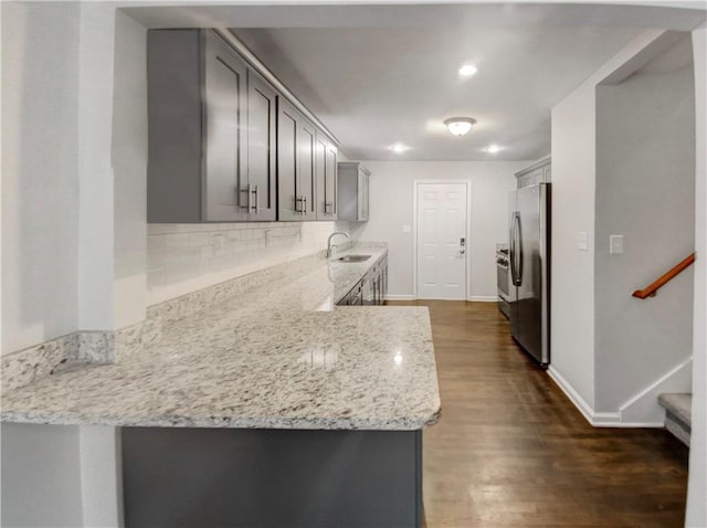 kitchen with gray cabinetry, sink, decorative backsplash, stainless steel fridge, and light stone countertops