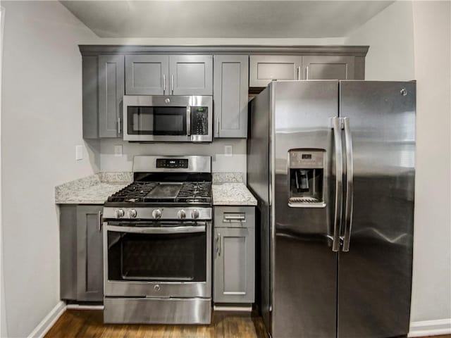 kitchen featuring gray cabinetry, light stone counters, dark hardwood / wood-style flooring, and stainless steel appliances