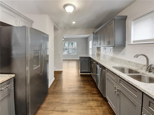 kitchen featuring backsplash, sink, gray cabinets, light stone countertops, and appliances with stainless steel finishes