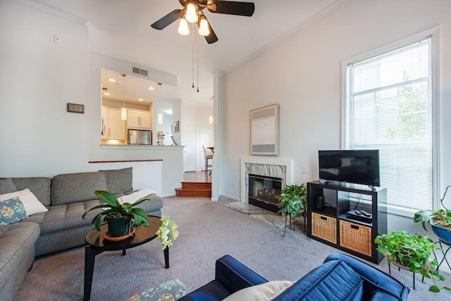 carpeted living area with ceiling fan, visible vents, ornamental molding, and a high end fireplace