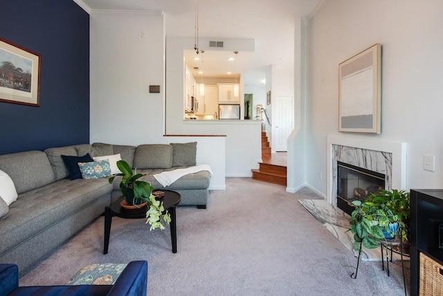 living area with visible vents, crown molding, stairs, light carpet, and a high end fireplace