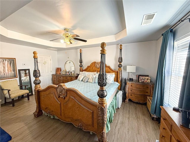 bedroom featuring light wood-type flooring, ceiling fan, visible vents, and a raised ceiling