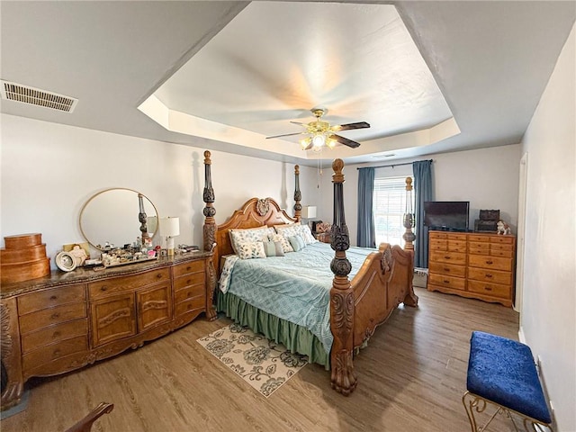 bedroom with ceiling fan, a tray ceiling, light wood-type flooring, and visible vents