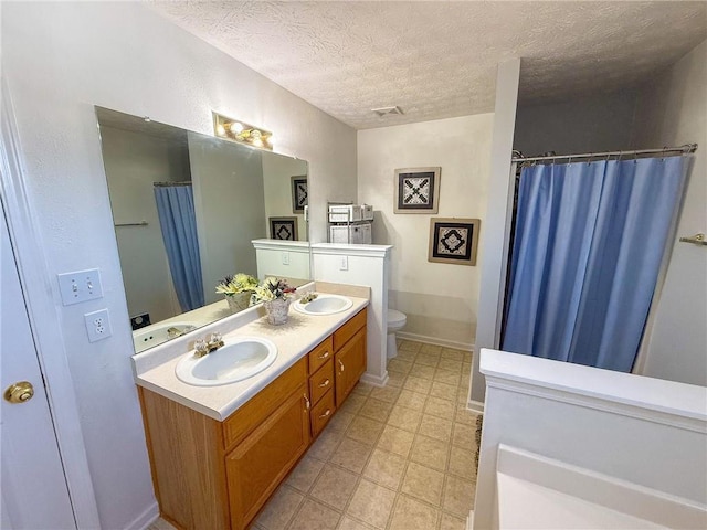 bathroom featuring a textured ceiling, double vanity, a sink, and toilet