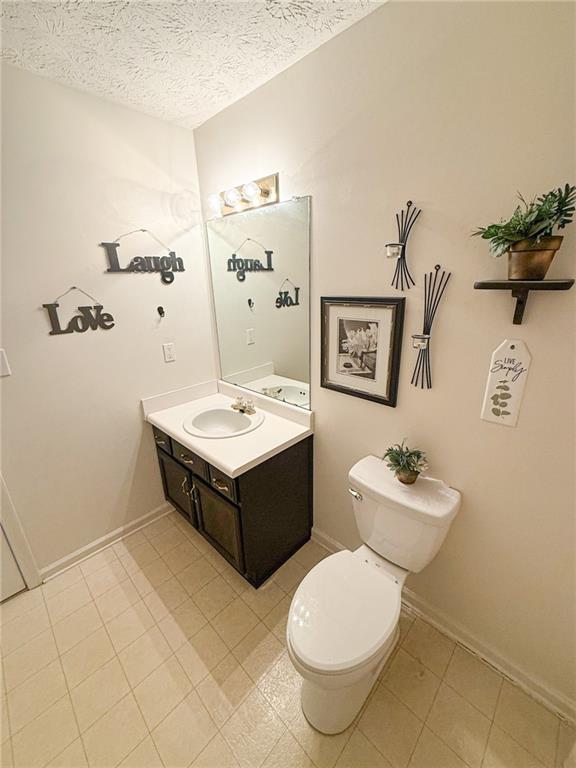 half bathroom featuring baseboards, toilet, vanity, and a textured ceiling