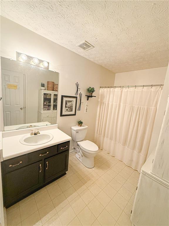 bathroom with visible vents, vanity, toilet, and a textured ceiling