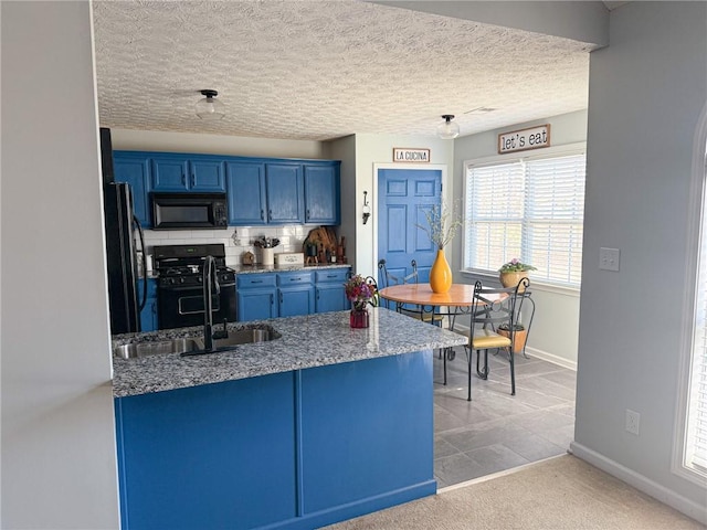 kitchen with a peninsula, a sink, baseboards, blue cabinetry, and black appliances