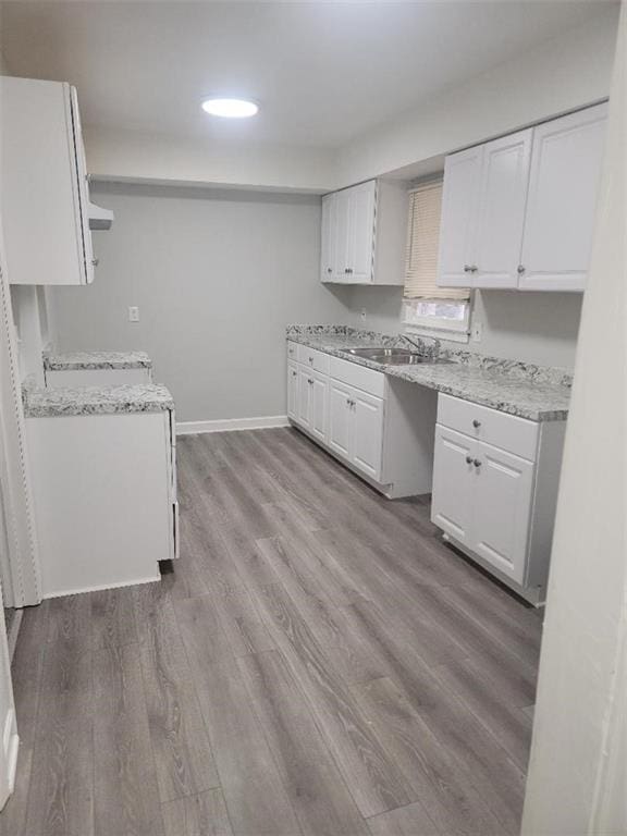 kitchen featuring light wood-type flooring, light stone counters, sink, white cabinets, and range hood