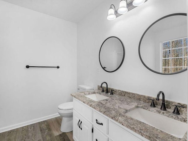 bathroom featuring double vanity, a sink, toilet, and wood finished floors