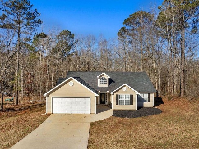 view of front of house with a front yard, a forest view, driveway, and an attached garage