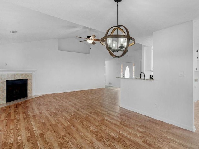 unfurnished living room featuring baseboards, a tile fireplace, vaulted ceiling, light wood-style floors, and ceiling fan with notable chandelier